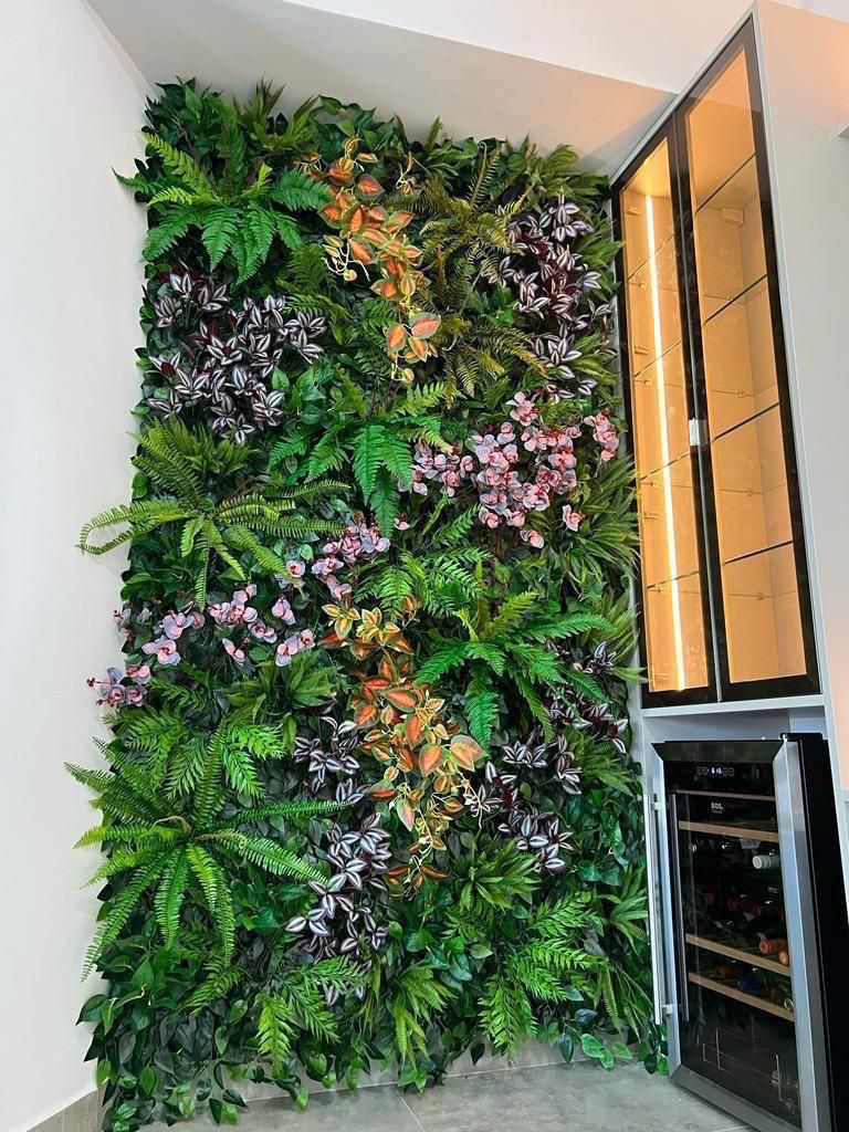 Jardim vertical artificial com parede totalmente coberta por folhagens densas e variadas, samambaias exuberantes, pothos e plantas trepadeiras em tons de verde intenso, ambiente interno com iluminação natural difusa, composição exuberante e tridimensional, fotografia realista de interiores